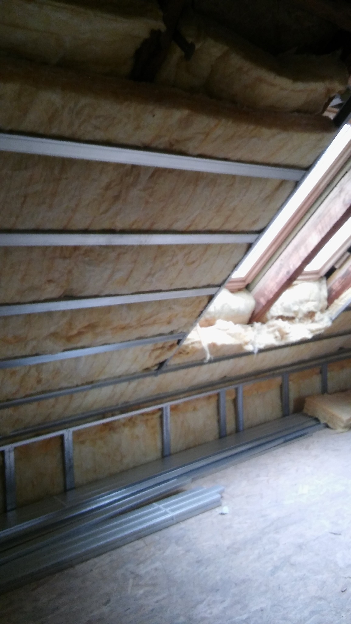 Izolacja poddasza wełną mineralną z widoczną konstrukcją metalową i oknem dachowym w trakcie montażu.