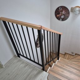 MAR - STAL MAREK LIS - Nowoczesna balustrada schodowa z czarnymi, pionowymi prętami i drewnianym pochwytem, widok z góry na drewniane schody z nakładkami dywanowymi i dekoracją ścienną.