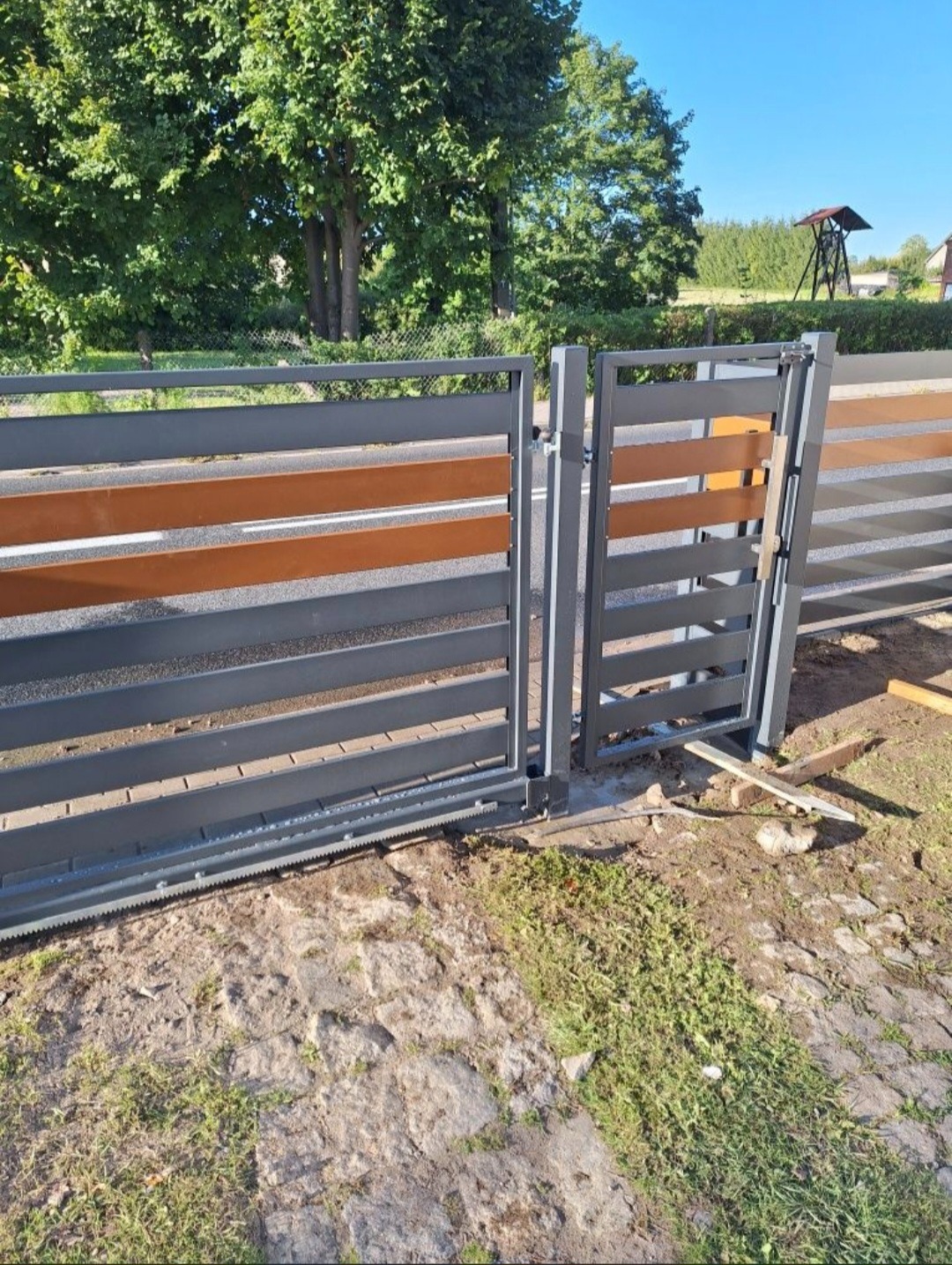 Nowoczesna brama przesuwna z poziomymi panelami w odcieniach szarości i brązu, automatyka widoczna u dołu. Realizacja w Borne Sulinowo.