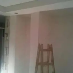 Wnętrze w trakcie prac wykończeniowych, ściany po nałożeniu warstwy wyrównującej, widoczna drewniana drabina oparta o ścianę, przygotowanie do dalszych prac.