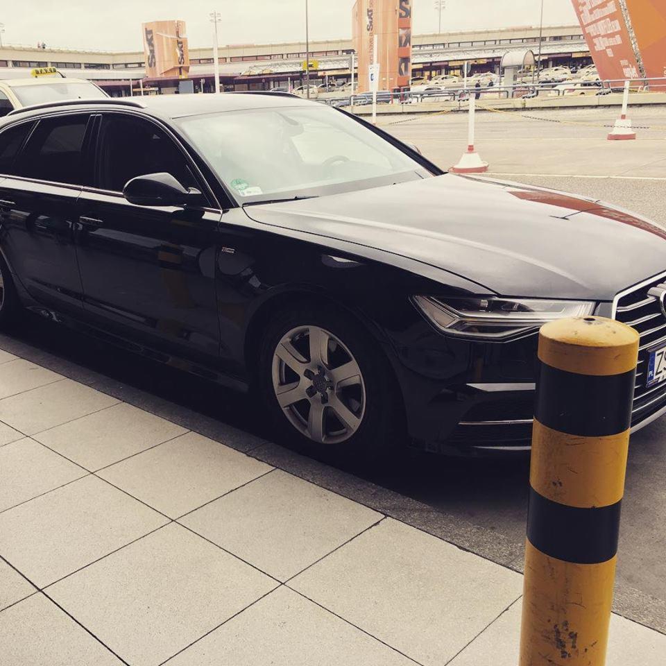Czarny samochód osobowy Audi kombi zaparkowany przy lotnisku, widoczne oznaczenia wypożyczalni Sixt w tle.