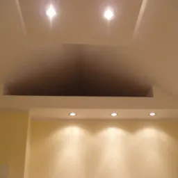 Nowoczesny sufit podwieszany z oświetleniem punktowym, jasne ściany, minimalistyczny design. Nietypowy kształt sufitu.