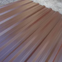 Brązowy arkusz blachy trapezowej z widocznymi przetarciami na krawędziach, leżący na szarym, betonowym podłożu.