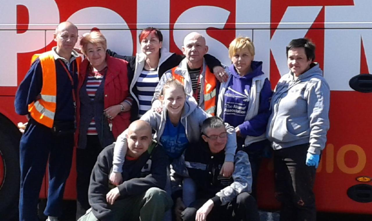 Grupa osób w kamizelkach odblaskowych pozuje na tle czerwonego autobusu z napisem, prawdopodobnie pracownicy firmy sprzątającej po akcji.