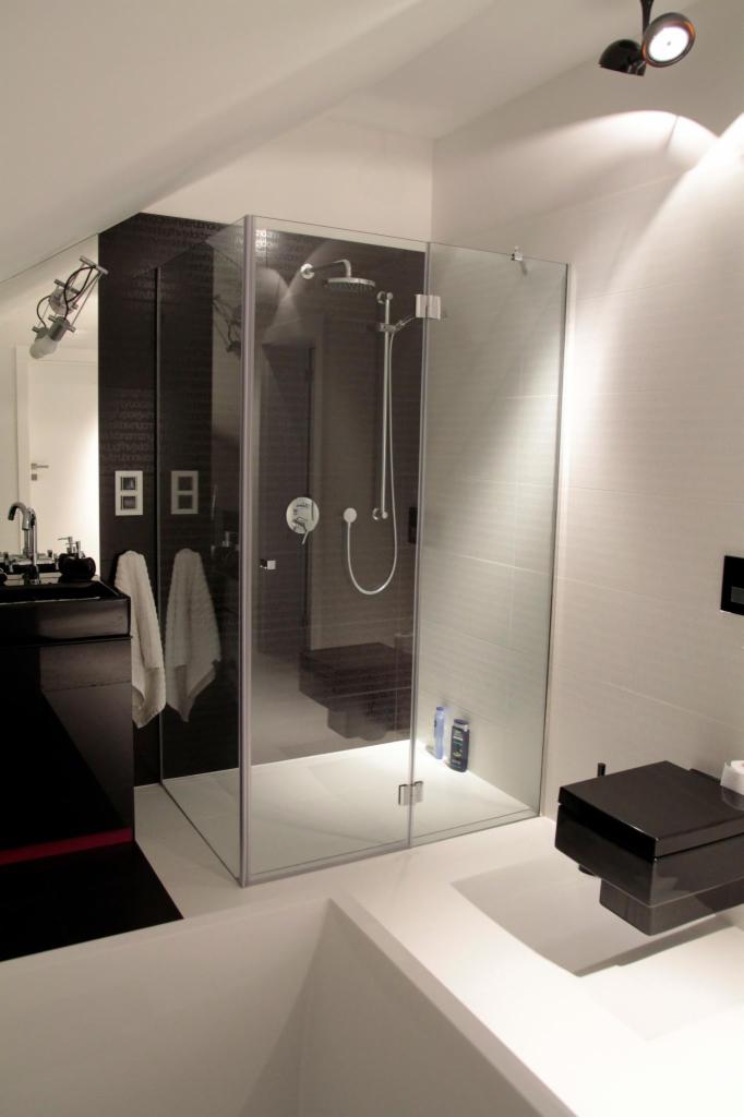 Nowoczesna kabina prysznicowa ze szklanymi drzwiami, minimalistyczna łazienka w czerni i bieli, oświetlenie punktowe, widoczna armatura i akcesoria łazienkowe.
