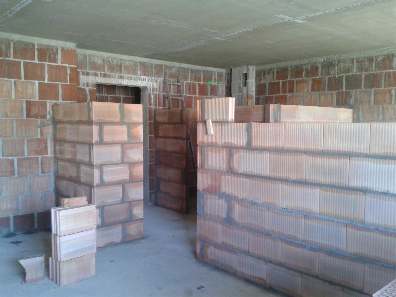 Wznoszenie ścian działowych z bloczków ceramicznych w surowym wnętrzu. Widoczne bloczki, zaprawa, betonowy strop i drabina oparta o ścianę.