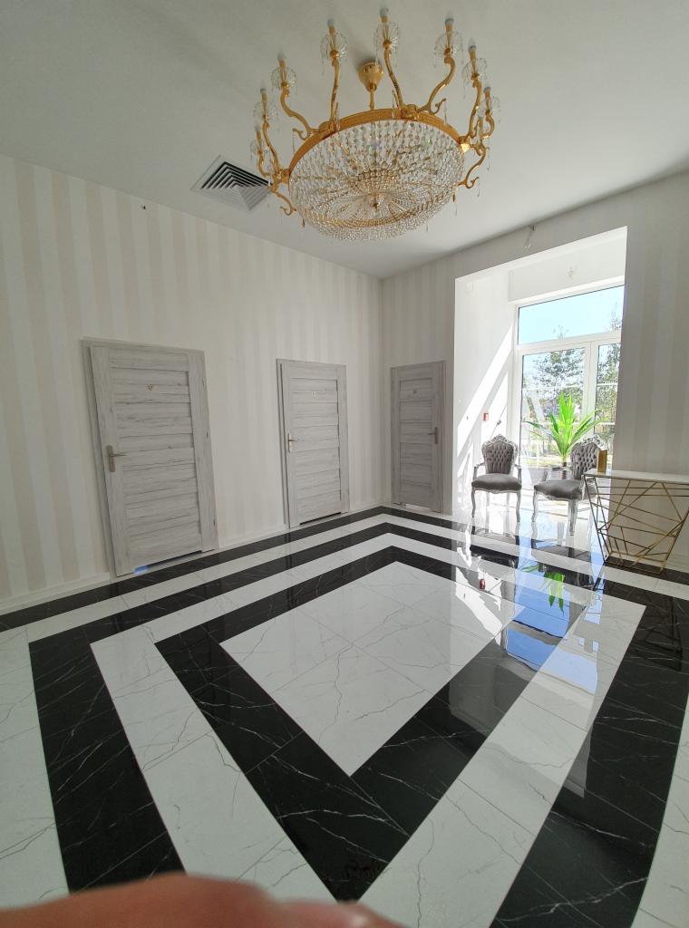 Eleganckie wnętrze z czarno-białą marmurową podłogą w geometryczny wzór, kryształowy żyrandol, trzy drewniane drzwi i dwa fotele w stylu vintage przy oknie.