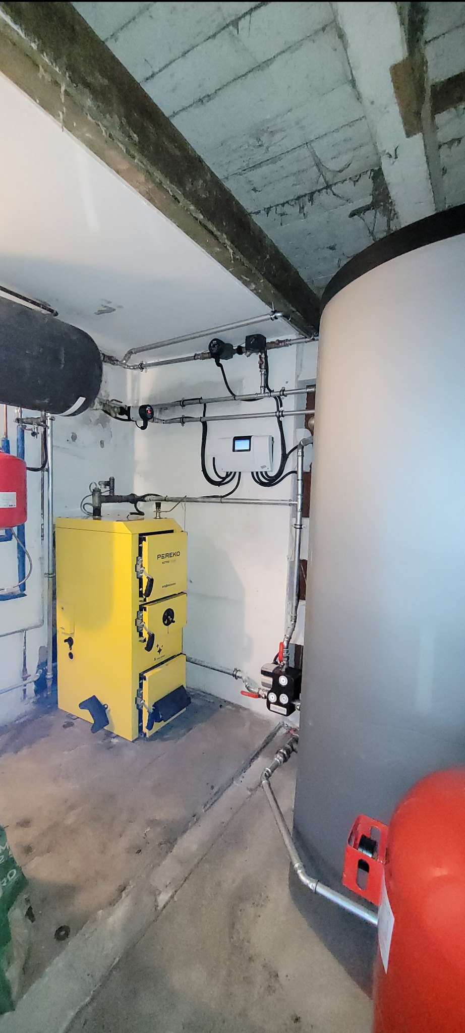 Żółty piec marki Pereko Retro w kotłowni w Darłowie, widoczne rury instalacji grzewczej i zbiornik buforowy.