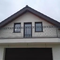 Balkon z kutą balustradą w kolorze grafitowym, widok z dołu, zadaszenie nad garażem.