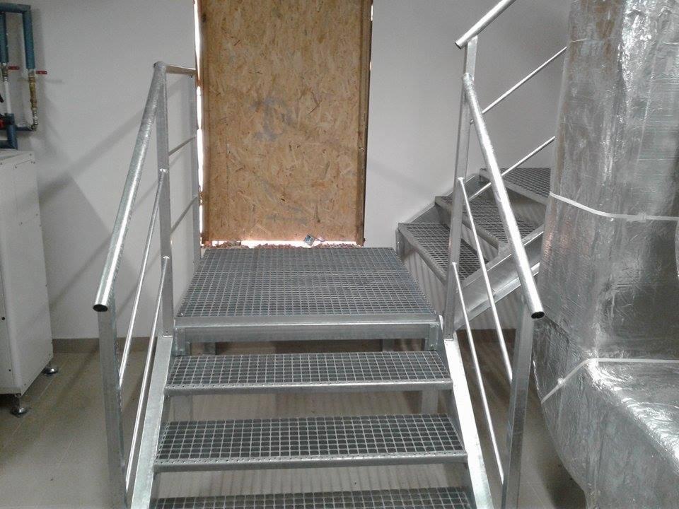 Metalowe schody kratowe z poręczami, widoczne zabezpieczone urządzenie w folii