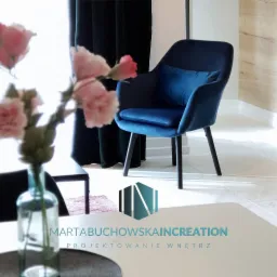 Niebieski, welurowy fotel z poduszką w nowoczesnym wnętrzu, ciemne zasłony w tle, kwiaty w wazonie na pierwszym planie, logo firmy projektującej wnętrza w dolnej części zdjęcia.