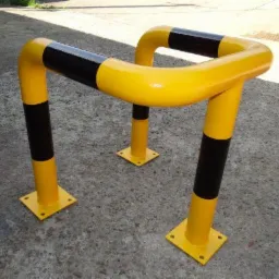 Metalowa bariera ochronna w kolorze żółto-czarnym, zabezpieczająca przed uszkodzeniami. Solidna konstrukcja na betonowym podłożu, widoczna z bliska.