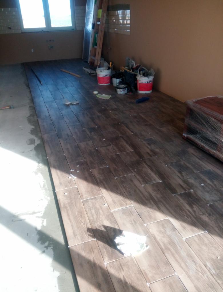 Układanie podłogowych płytek imitujących drewno w Gnieźnie, widoczne narzędzia i materiały budowlane, etap prac wykończeniowych.