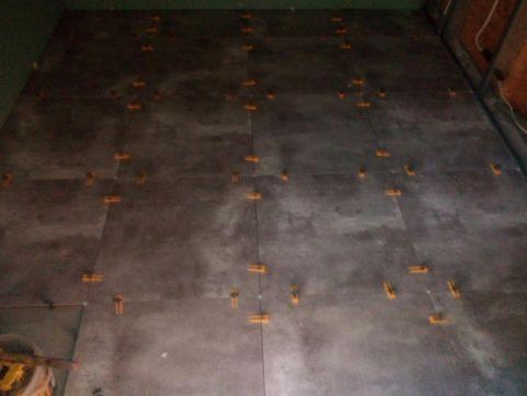 Układanie szarych płytek podłogowych z pomarańczowymi krzyżykami dystansowymi, widok z góry na fragment podłogi w trakcie prac wykończeniowych.