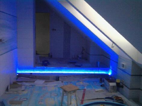 Łazienka w trakcie remontu z podświetleniem LED wzdłuż podłogi i na suficie. Widoczny fragment poddasza i narzędzia. Ujęcie z niskiego kąta.