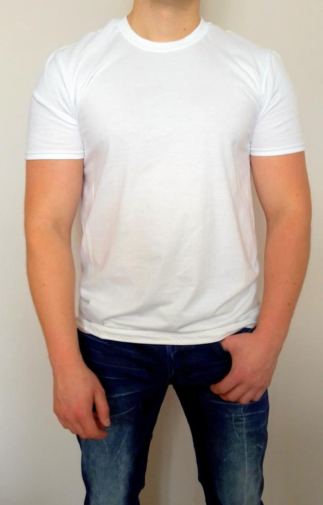 Mężczyzna w białej koszulce z krótkim rękawem i dżinsach, stojący na tle jasnej ściany. Idealny materiał do prezentacji nadruków.