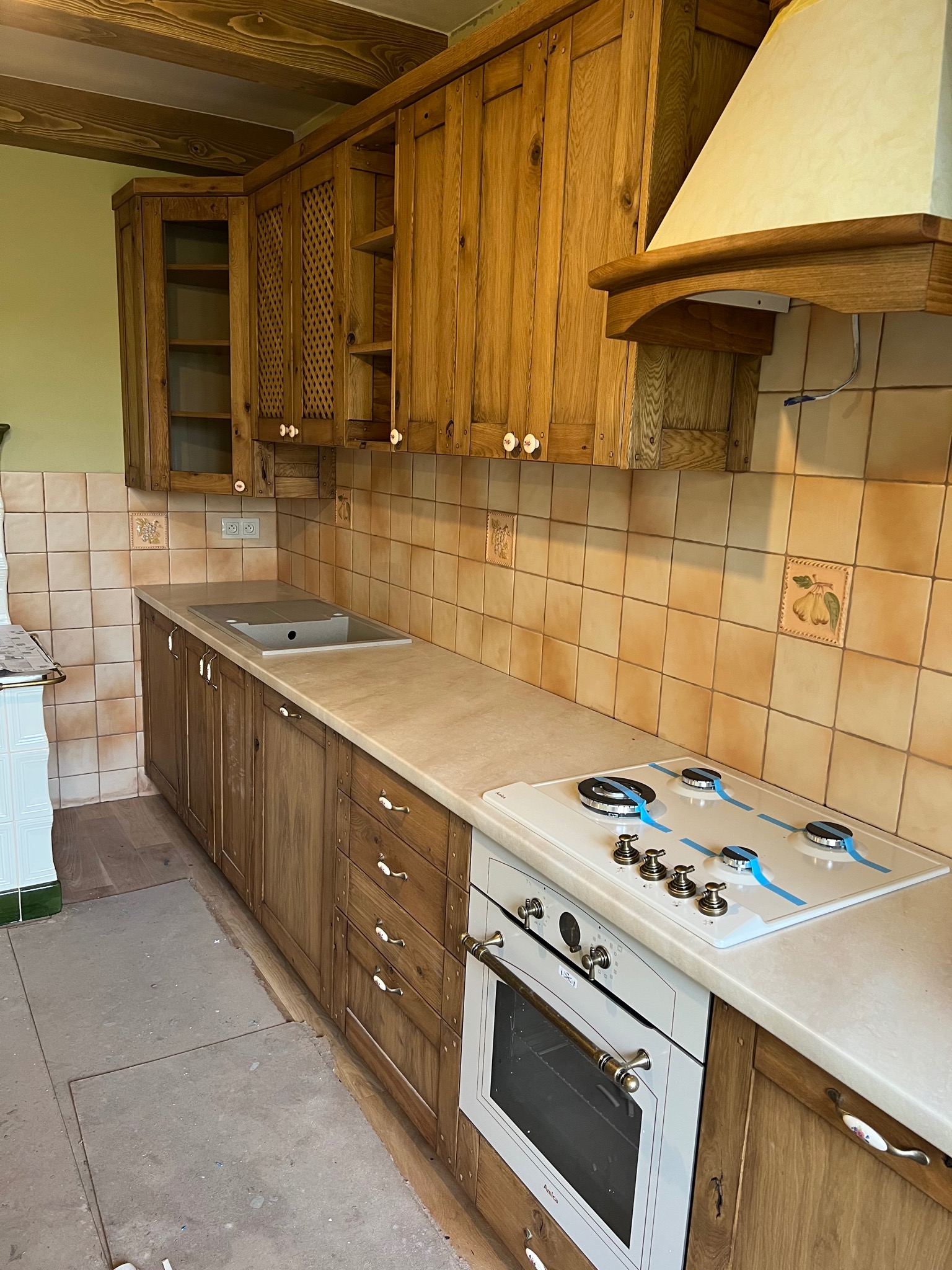 Rustykalna kuchnia z drewnianymi szafkami, beżowymi płytkami z motywami owoców i białą kuchenką z zabezpieczeniami.