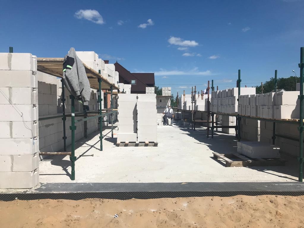 Budowa domu z bloczków betonu komórkowego: widok na wznoszone ściany z rusztowaniami, pracownik w oddali, świeży fundament w pierwszym planie.