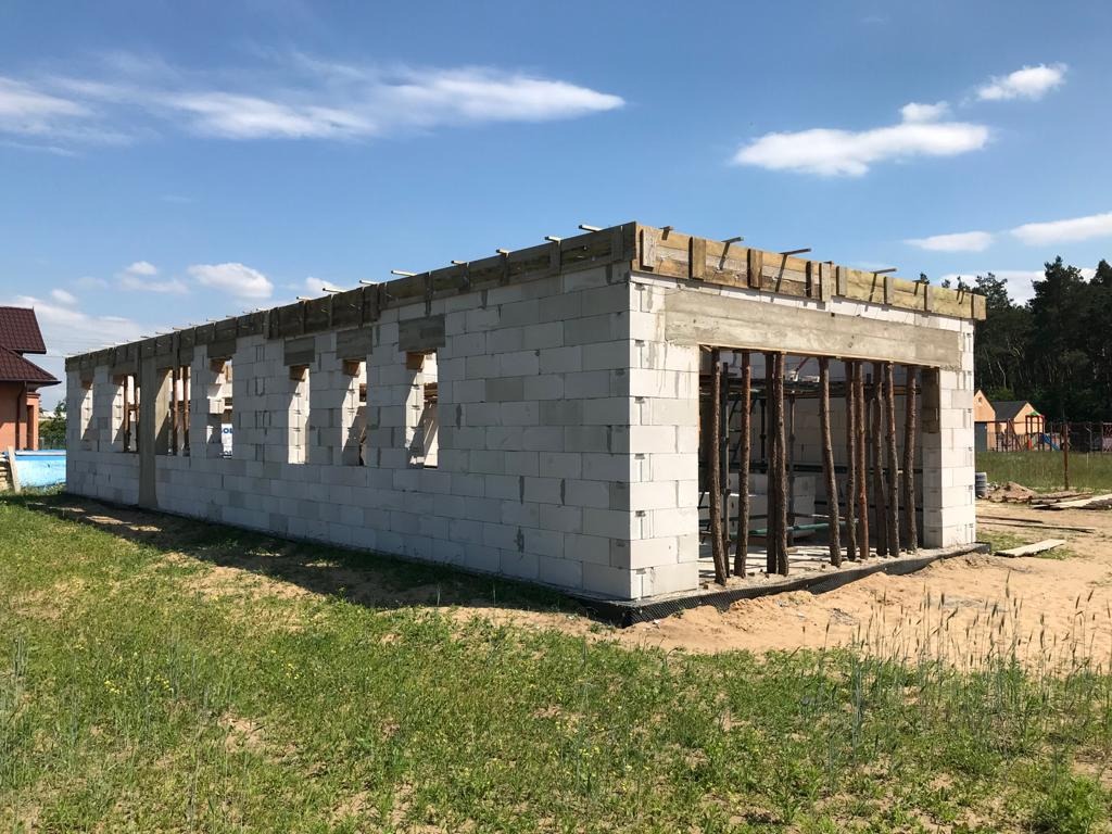 Wznoszenie ścian z betonu komórkowego Ytong z widocznym zbrojeniem nadproży okiennych i deskowaniem stropu garażu, w tle zabudowa jednorodzinna i błękitne niebo.