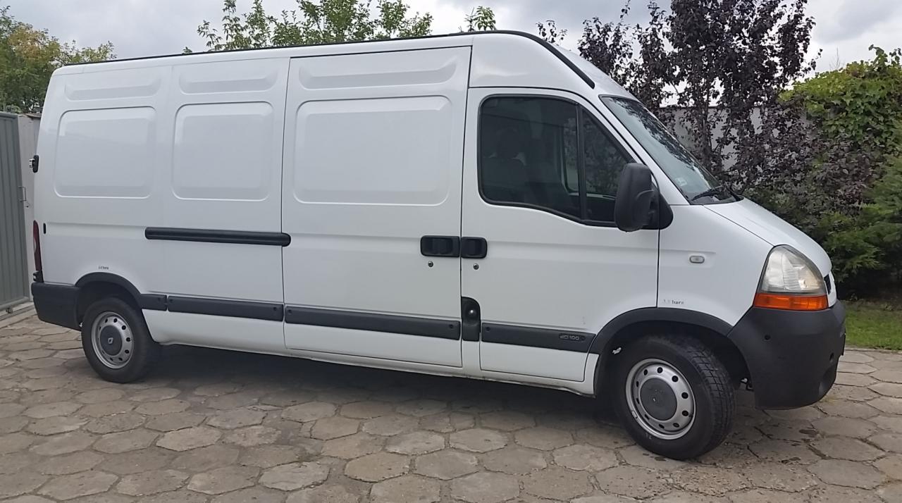 Biały bus dostawczy Renault Master na brukowanym podjeździe, z widocznymi detalami nadwozia i oponami, na tle zieleni.