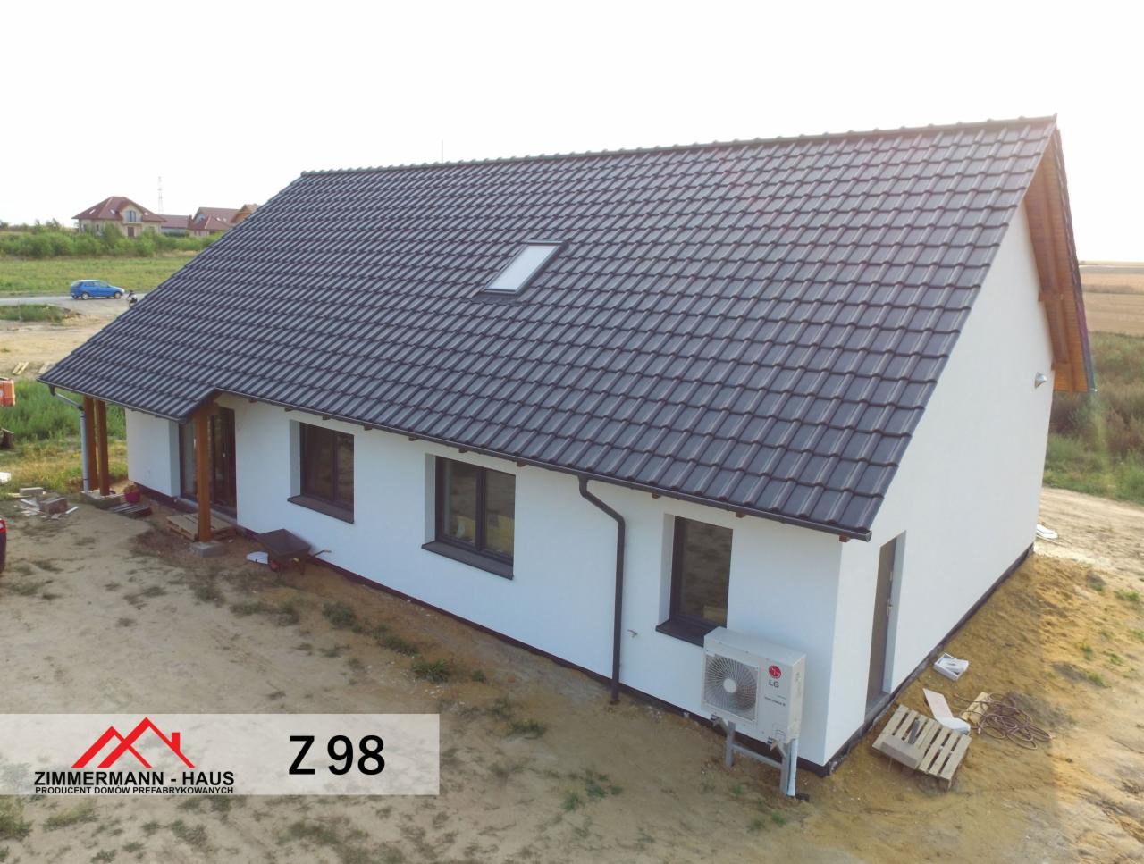 Gotowy dom szkieletowy z ciemną dachówką, widoczne okna z czarnymi ramami, klimatyzator LG na zewnątrz, teren wokół domu jeszcze niezagospodarowany.