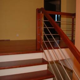 Jscarpentry - Schody z drewnianymi stopniami i poręczą z metalowymi prętami, oświetlone ciepłym światłem, widok z dołu, podkreślona precyzja wykonania.