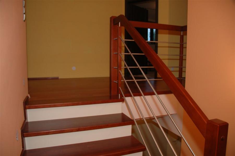 Schody z drewnianymi stopniami i poręczą z metalowymi prętami, oświetlone ciepłym światłem, widok z dołu, podkreślona precyzja wykonania.