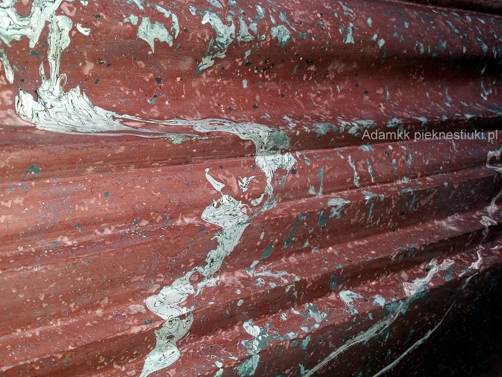 Fragment ściany z dekoracyjnym tynkiem w odcieniach czerwieni i bieli, imitującym marmur, z widoczną strukturą i żyłkowaniem.