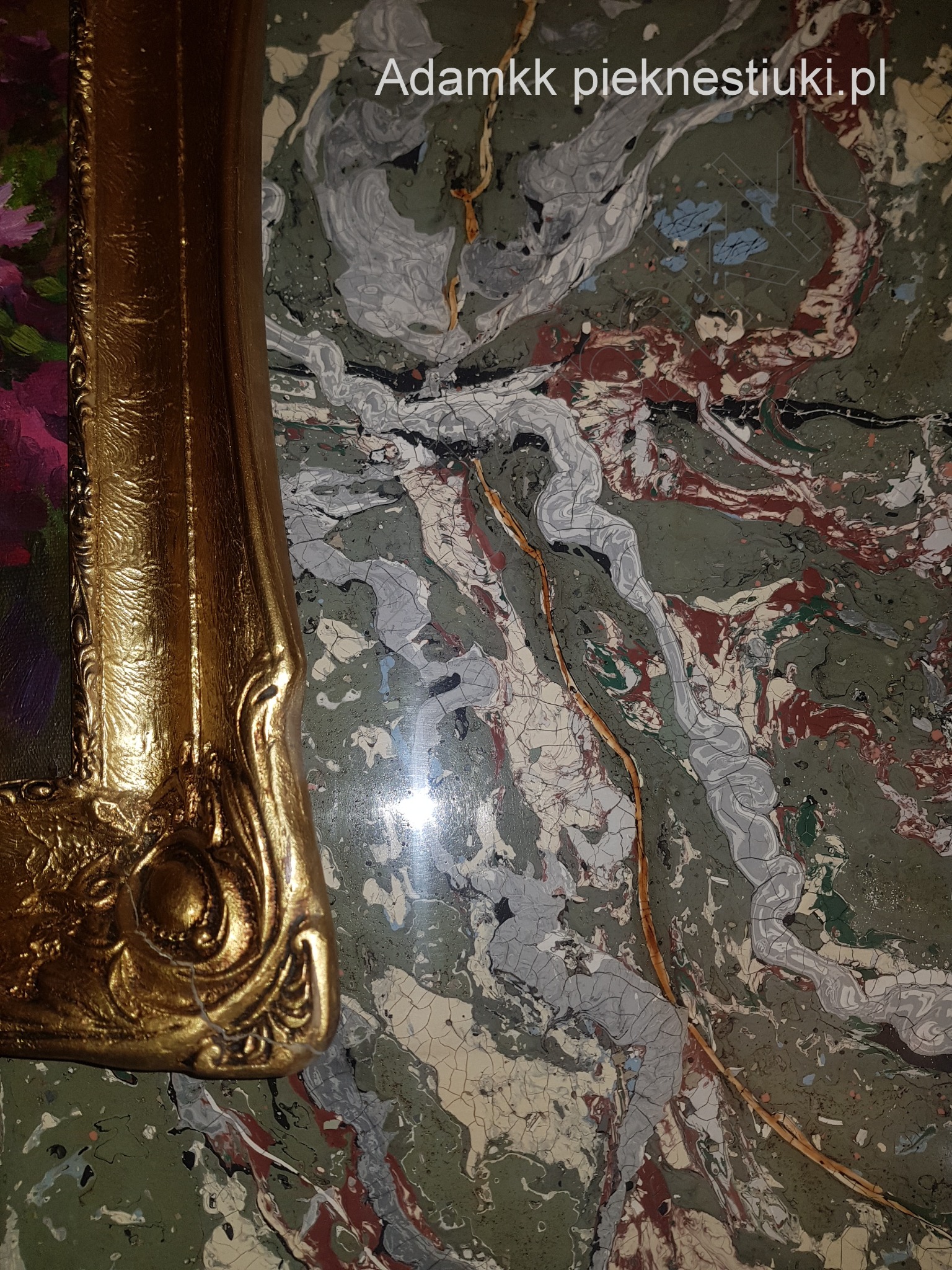 Fragment ściany z efektem stiuku marmurowego w odcieniach zieleni, szarości i czerwieni, z widocznym narożnikiem złotej ramy obrazu po lewej stronie. Na powierzchni widoczny adres strony internetowej.
