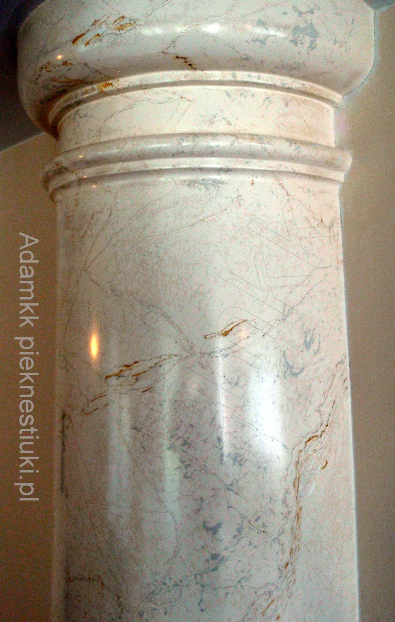 Detal kolumny wykończonej stiukiem imitującym marmur z widocznymi żyłami i delikatnym połyskiem, wykonana w jasnej kolorystyce.