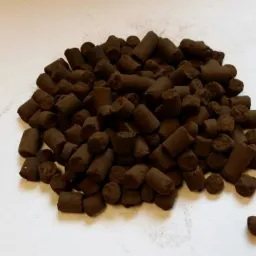 Kompaktowa sterta ciemnobrązowego agropelletu na jasnym tle. Widoczne cylindryczne kształty i tekstura granulatu. Pojedynczy granulat oddzielony od reszty.