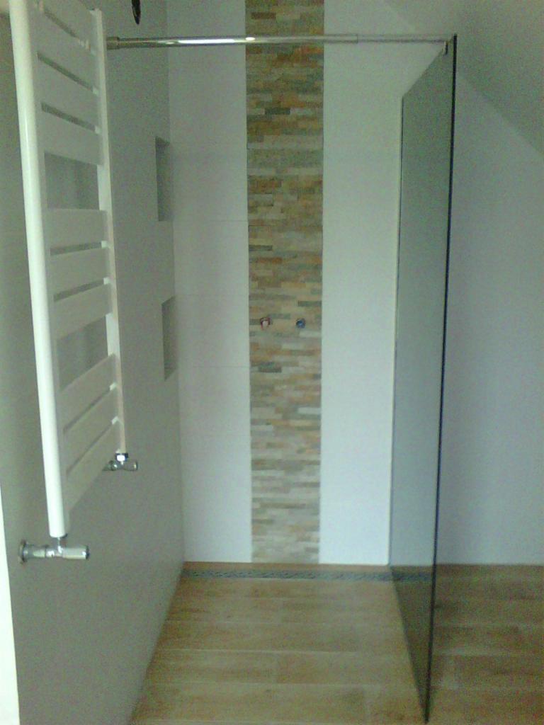 Nowoczesna kabina prysznicowa walk-in z grzejnikiem drabinkowym i akcentem kamiennej mozaiki na ścianie, wykończona płytkami imitującymi drewno na podłodze.