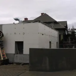 Pracownik na drabinie, w trakcie prac wykończeniowych zewnętrznych budynku z płyt kartonowo-gipsowych, widoczne łączenia płyt i szpachlowanie narożnika.