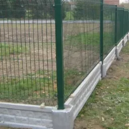 Zielone ogrodzenie panelowe z podmurówką z szarej cegły betonowej, widoczne z boku na zewnątrz, w tle trawa i drzewa.