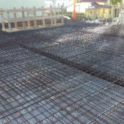 Zbrojenie stropu budynku w trakcie budowy, widoczne siatki i drewniany element konstrukcyjny, przygotowane do zalania betonem. Perspektywa z góry.