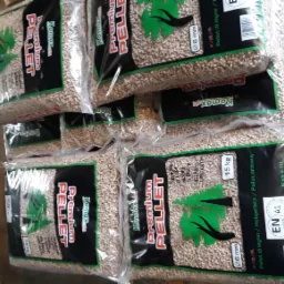 Stos worków z pelletem drzewnym Komax Premium, widoczne oznaczenia certyfikacji i specyfikacji produktu, ułożone na drewnianej palecie w magazynie.