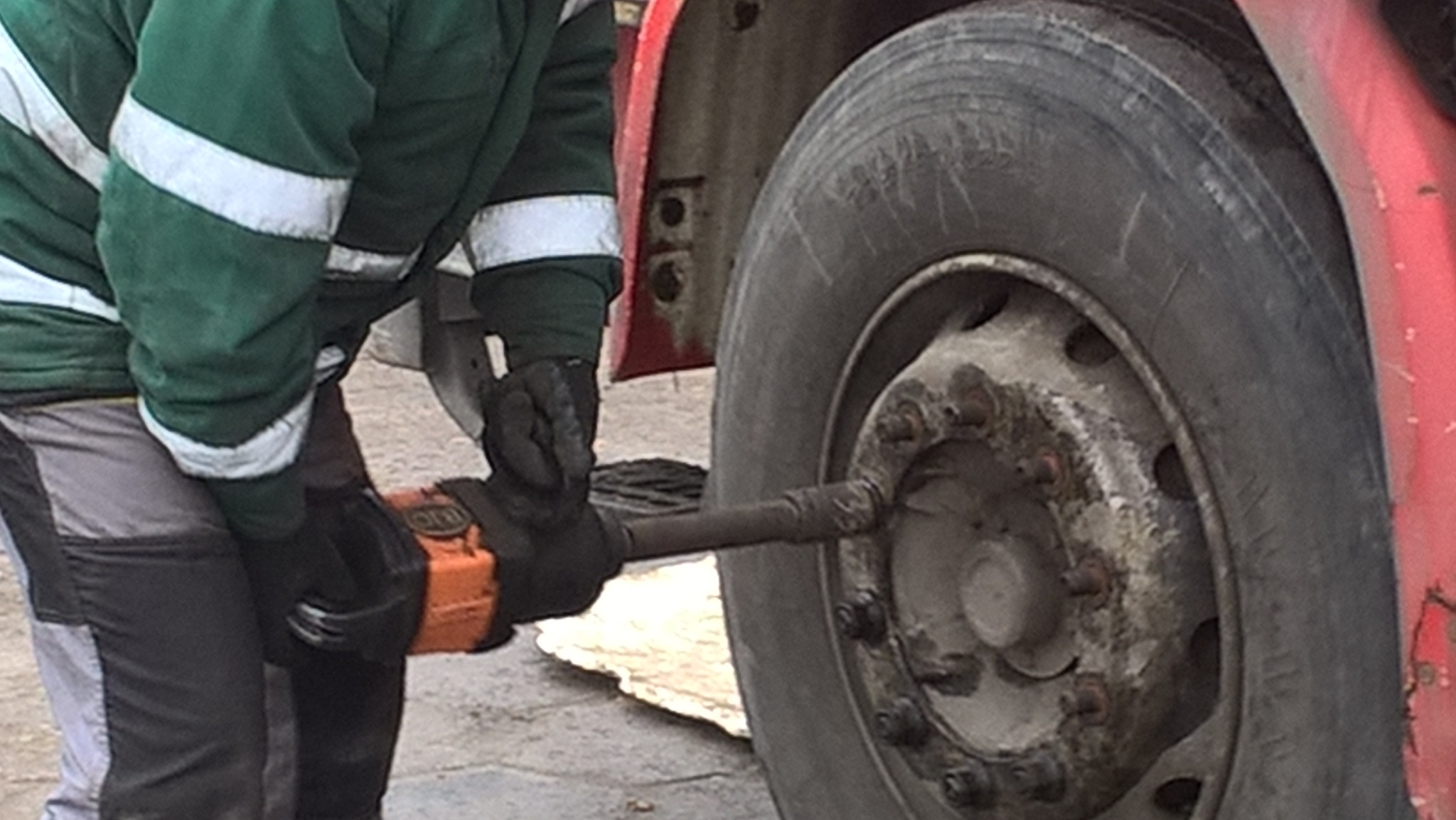 Pracownik w odzieży roboczej wymienia koło w czerwonej ciężarówce za pomocą klucza pneumatycznego.