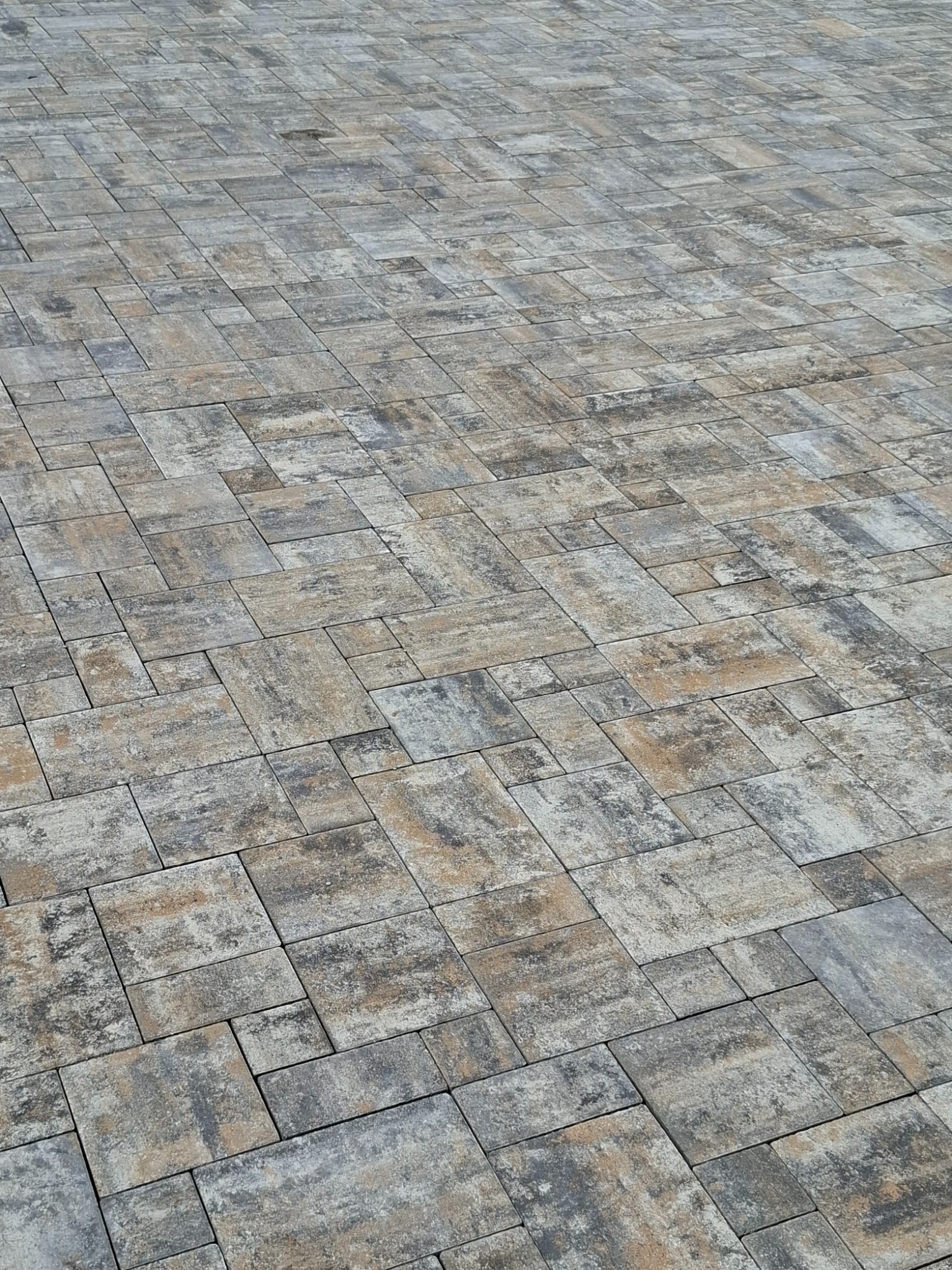 Ułożona kostka brukowa w odcieniach szarości i beżu, tworząca wzór na dużej powierzchni. Widok z góry, ukazujący regularność i estetykę wykonania.