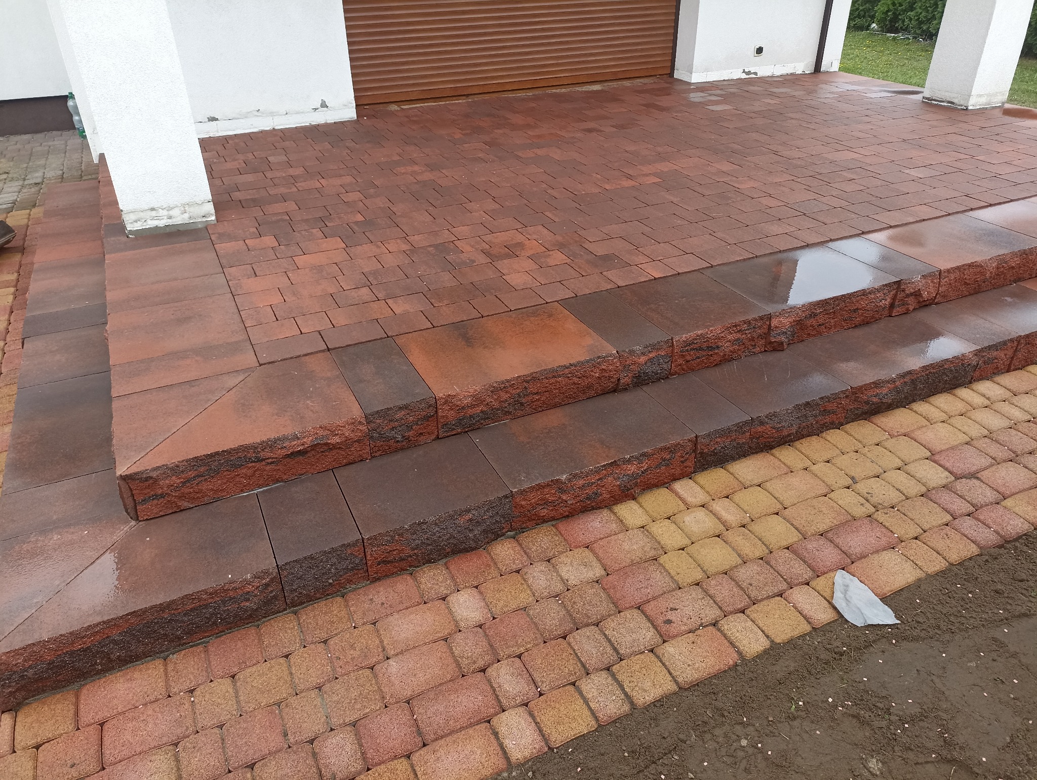 Ułożona kostka brukowa w odcieniach brązu i żółci tworząca schody i podjazd. Widoczne detale faktury kostki i staranne wykonanie.