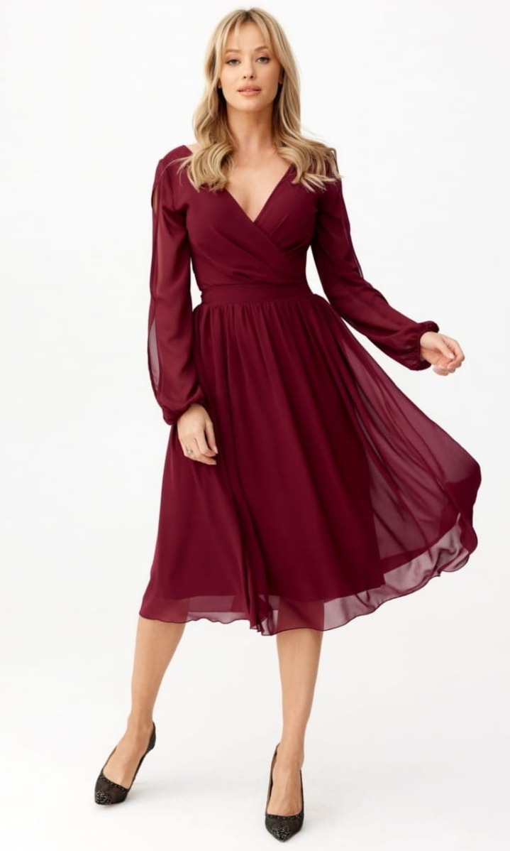 Kobieta w bordowej, szyfonowej sukience midi z długim, prześwitującym rękawem, pozująca na białym tle. Sukienka z dekoltem w kształcie litery V i wiązaniem w pasie. Uzupełnieniem stylizacji są...