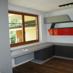 Wytwórnia Mebli Pabi-Mebel - Nowoczesne meble na wymiar w szarościach i czerwieni, zintegrowane z oknem. Minimalistyczne półki na ścianie i drewniana podłoga dodają charakteru wnętrzu.