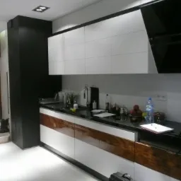 Nowoczesna kuchnia z białymi szafkami górnymi i dolnymi z drewnianym akcentem. Czarny blat i kolumna po lewej stronie. Minimalistyczny design, jasne wnętrze.