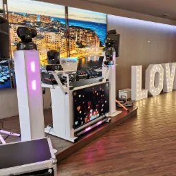 Stanowisko DJ-a z oświetleniem scenicznym i dekoracją LOVE z żarówkami, tło z widokiem na miasto, przygotowane do obsługi imprezy weselnej.