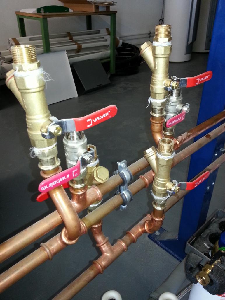 Miedziane rury połączone z zaworami i filtrami, instalacja wodna z czerwonymi uchwytami zaworów, srebrne mocowania rur, widok z bliska.