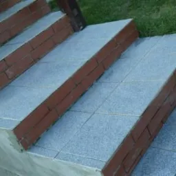 Wykończone płytkami schody zewnętrzne z ceglanym obrzeżem w Wojcieszowie. Widok z góry, zieleń w tle. Estetyczne ułożenie płytek, detale wykończenia.