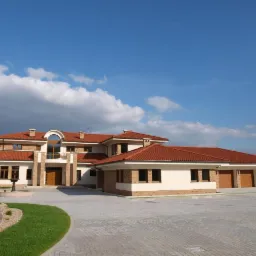 Rozległy, dwukondygnacyjny dom z czerwonym dachem i garażem na trzy auta. Jasna elewacja z ceglanymi akcentami. Brukowany podjazd, fontanna i zadbany trawnik.