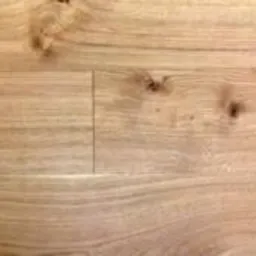 Jasny, dębowy blat drewniany z widocznymi słojami i sękami. Ciepłe oświetlenie podkreśla naturalną strukturę drewna.