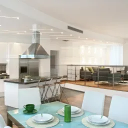 Jasne, przestronne wnętrze mieszkania z otwartą kuchnią, wyspą kuchenną z hokerami i salonem na podwyższeniu, oświetlenie punktowe na suficie, stół z nakryciem i zielonymi akcentami.