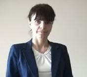 Portret kobiety w białej bluzce i granatowej marynarce na jasnym tle. Uśmiech, ciemne włosy z grzywką.