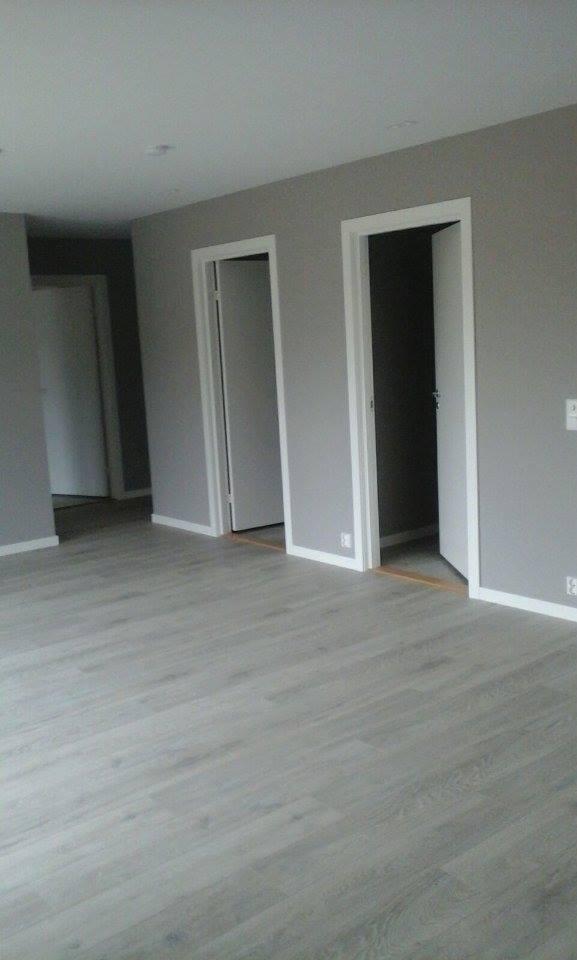 Wnętrze pomalowanego na szaro pokoju z jasną drewnianą podłogą i trzema parami drzwi z białymi ościeżnicami, z czego jedne drzwi są otwarte.